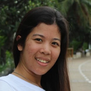 A cheerful woman outdoors on a palm-lined path, smiling as she enjoys her experience with KuyaPlay free bonus.